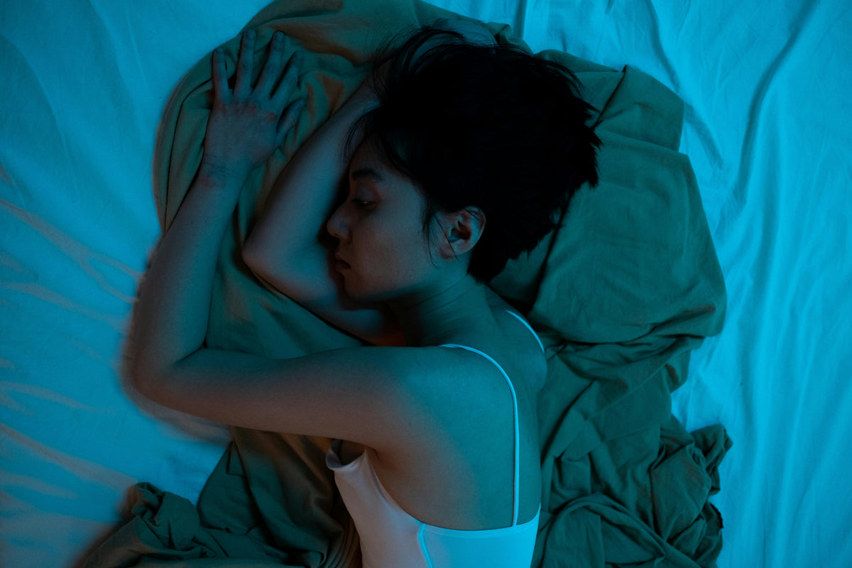 Woman laying in bed restlessly. The filter is a dark blue saturated blanket over photo